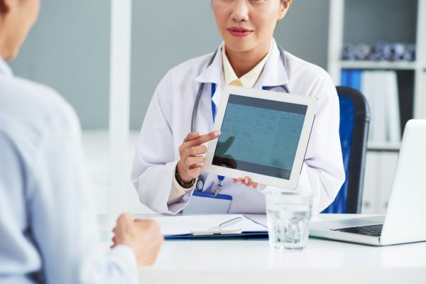 Eine Ärztin zeigt einem Patienten die Online-Terminplanung am Tablet
